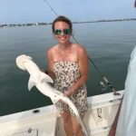 Woman holding a bonnethead shark caught on a fishing charter in Sarasota Bay, Florida, with the Sarasota skyline in the background