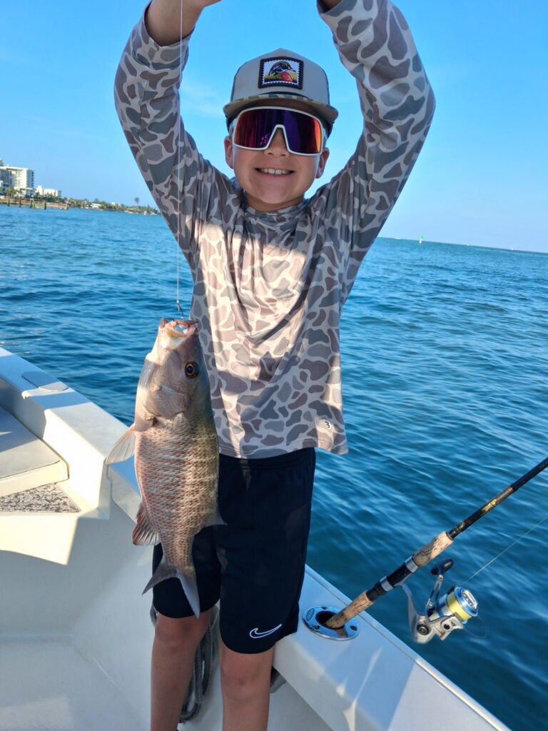 Young angler celebrating with a mangrove snapper caught on a family fishing charter in Sarasota Bay, Florida