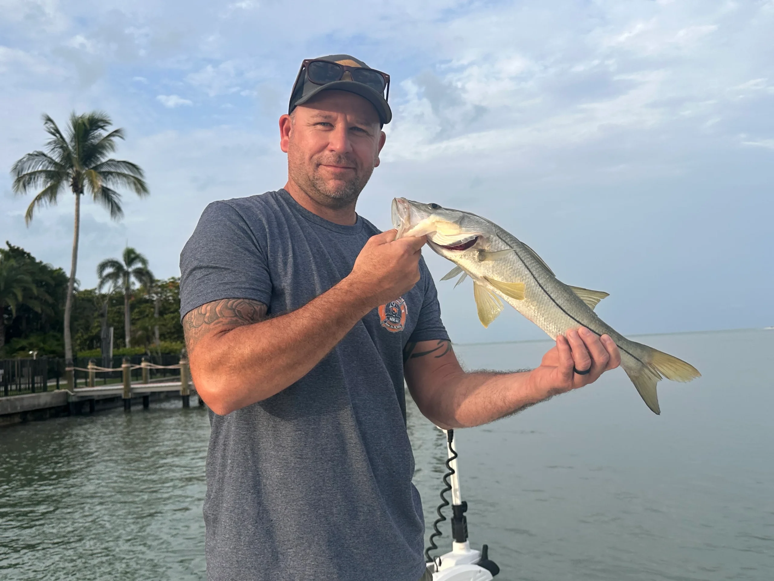 Angler holding a snook caught inshore on a fishing charter in Sarasota, Florida, with a dock and palm trees in the background