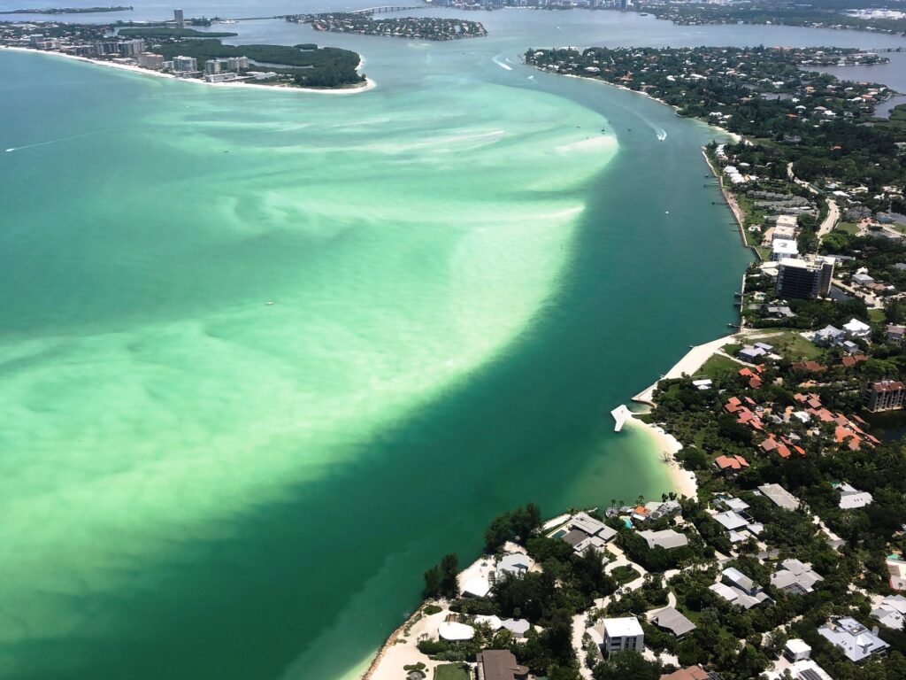 Aerial view of Sarasota coastal pass showing emerald green water, sandbars, and the channel connecting Sarasota Bay to the Gulf of Mexico