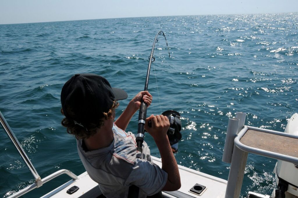 Young angler fighting a fish on a bent rod offshore in the Gulf of Mexico on a calm blue-water day out of Sarasota, Florida